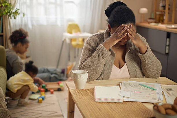 Parent at a kitchen table reviewing finances, child's activity gear in frame